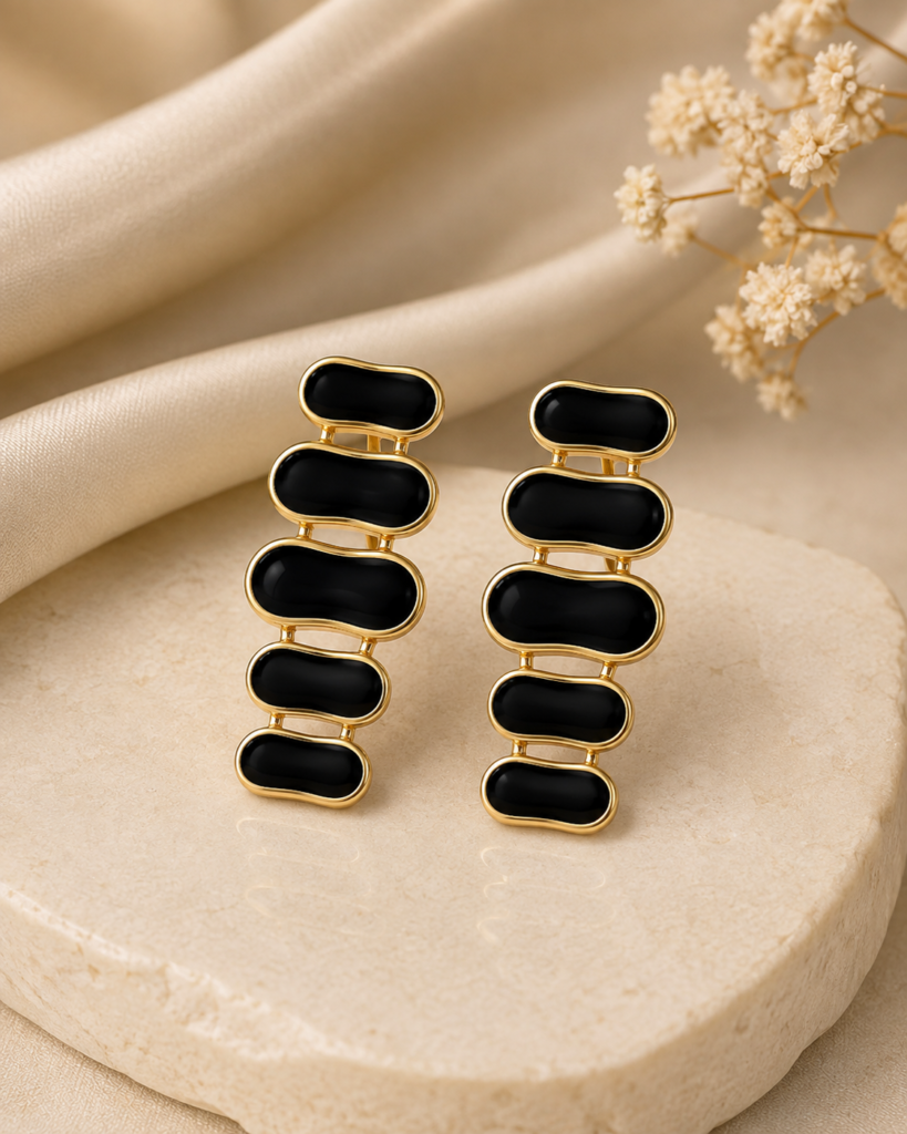 Black enamel gold-tone cascade drop earrings on a cream stone and satin background
