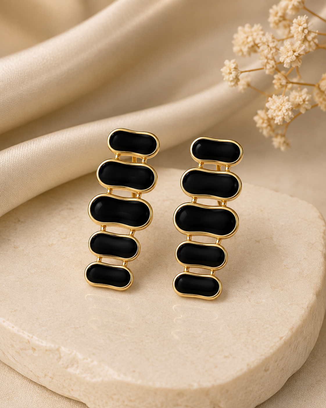 Black enamel gold-tone cascade drop earrings on a cream stone and satin background