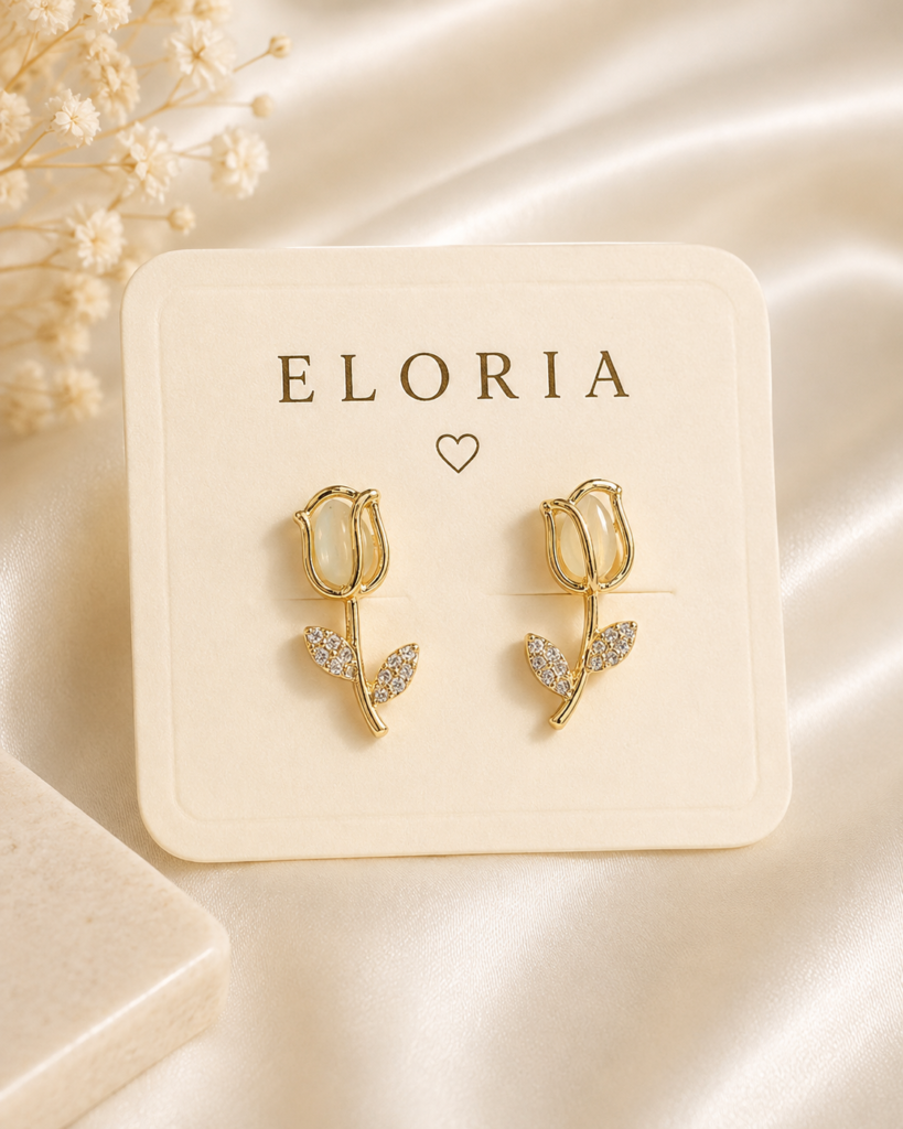 Gold-tone floral vine earrings with crystal leaf accents displayed on an ELORIA jewelry card over ivory satin.
