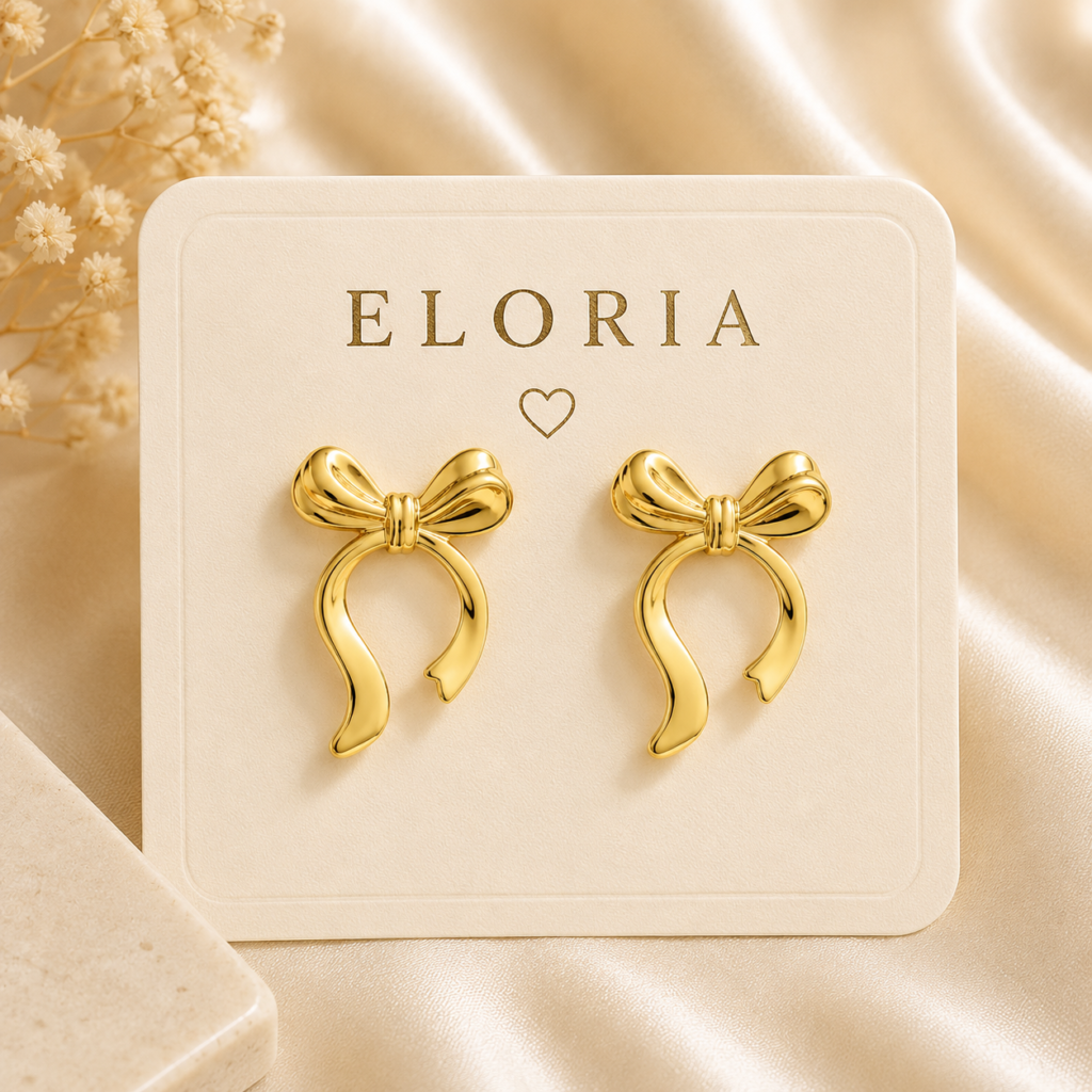 Gold-tone bow ribbon loop earrings displayed on a white jewelry card over champagne satin.