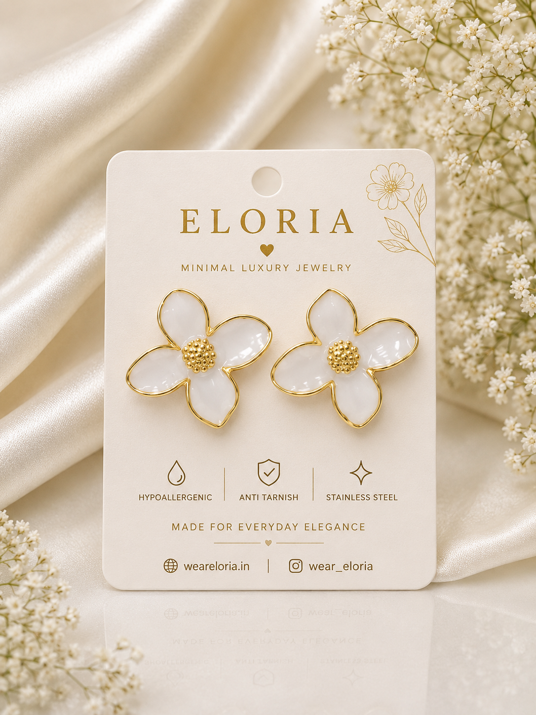ELORIA white flower-shaped earrings with gold outline and textured gold center displayed on luxury jewelry card