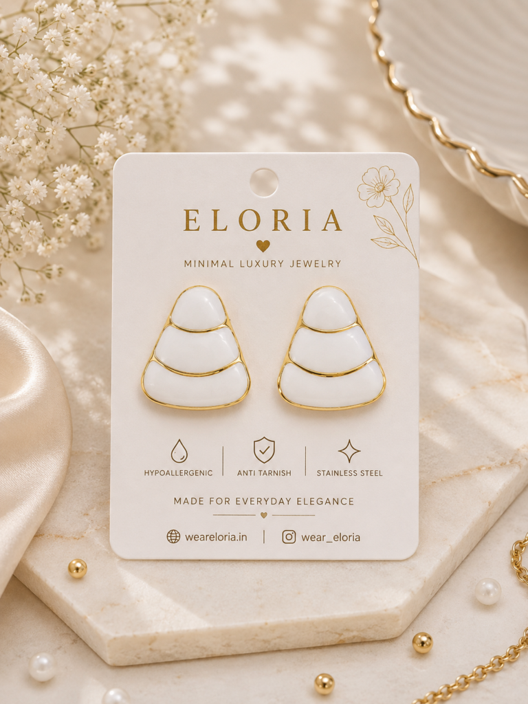 ELORIA white enamel tiered drop earrings with gold detailing displayed on a luxury jewelry card