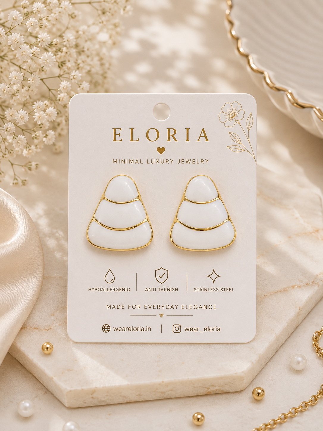 ELORIA white enamel tiered drop earrings with gold detailing displayed on a luxury jewelry card